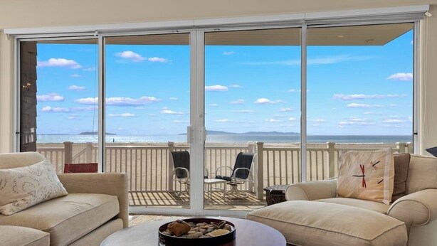 A balcony with a view of the beach, a sofa, a round table, and two chairs. - Beachfront abode with spacious deck, pool table, gas grill, smart TVs, & W/D (Oxnard)