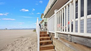 A beachfront property with a wooden staircase leading to a balcony, a clear view of the beach, and a sandy landscape. - Beachfront abode with spacious deck, pool table, gas grill, smart TVs, & W/D (Oxnard)
