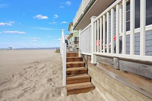 Ein Strandgrundstück mit einer Holztreppe, die zu einem Balkon führt, mit freiem Blick auf den Strand und einer sandigen Landschaft.
