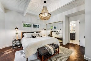 Ein Schlafzimmer mit einem großen Bett, einem Nachttisch, einer Bank, einem Spiegel und einer Chandelier.