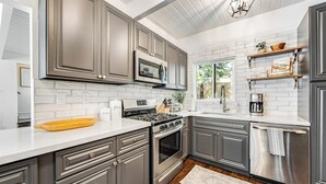 Una cocina moderna con armarios grises, encimera blanca, estufa de acero inoxidable y microondas.