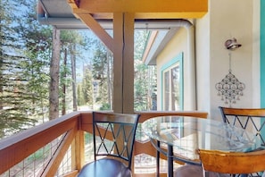 Ein Balkon mit Glastisch und Stühlen, der auf eine bewaldete Landschaft blickt.