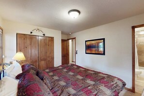 A bedroom with a bed, a wooden wardrobe, a framed picture on the wall, and a staircase. - Los Pinos #C14 with private balcony and garage, quick walk to Snowflake lift (Breckenridge)