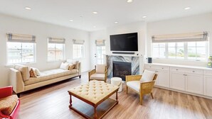 A spacious living room with a sofa, chairs, a coffee table, a fireplace, and a television mounted above it. - Beautiful Oceanview home with outdoor grill and spacious rooftop (Pismo Beach)