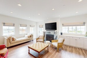 A spacious living room with a sofa, chairs, a coffee table, a fireplace, and a television mounted above it. - Beautiful Oceanview home with outdoor grill and spacious rooftop (Pismo Beach)