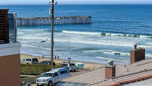 A coastal view with a pier extending into the ocean, a beach with parked cars, and a building with a rooftop. - Beautiful Oceanview home with outdoor grill and spacious rooftop (Pismo Beach)