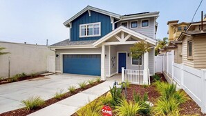 A two-story house with a garage, a white picket fence, and a landscaped front yard. - Beautiful Oceanview home with outdoor grill and spacious rooftop (Pismo Beach)