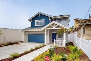 A two-story house with a garage, a white picket fence, and a landscaped front yard. - Beautiful Oceanview home with outdoor grill and spacious rooftop (Pismo Beach)