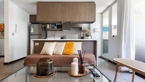 Ett modernt hotellrum med en säng, ett soffbord i glas, en liten köksdel och utsikt över omgivningarna.