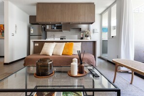 A modern hotel room with a bed, a glass coffee table, a kitchen area, and a view of the outside. - Modern Apartment with Excellent Location in Las Condes (Las Condes)