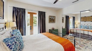 A bedroom with a bed, a ceiling fan, a dresser, a mirror, and a view of the outdoors. - The Avenue: Charming hideaway with private deck & peeks of ocean, near downtown (Ventura)