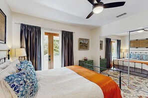 Ein Schlafzimmer mit Bett, Deckenventilator, Kommode, Spiegel und Blick ins Freie.