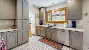 A kitchen with grey cabinets, a white countertop, a window with a wooden frame, and a tiled floor. - The Avenue: Charming hideaway with private deck & peeks of ocean, near downtown (Ventura)