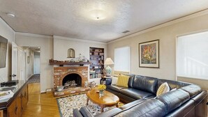 A living room with a fireplace, leather sofa, coffee table, and a bookshelf. - The Avenue: Charming hideaway with private deck & peeks of ocean, near downtown (Ventura)