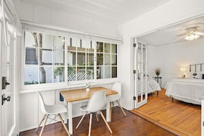 A room with a wooden dining table, white chairs, a bed, and a large window with a view of the outdoors. - Coastal retreat with patio, sun deck, & kitchenette - 2-minute walk to beach (Santa Barbara)