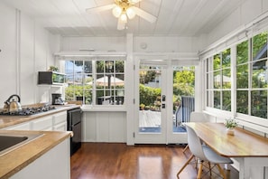 A kitchen with white cabinetry, a stove, and a dining area with a table and chairs. - Coastal retreat with patio, sun deck, & kitchenette - 2-minute walk to beach (Santa Barbara)