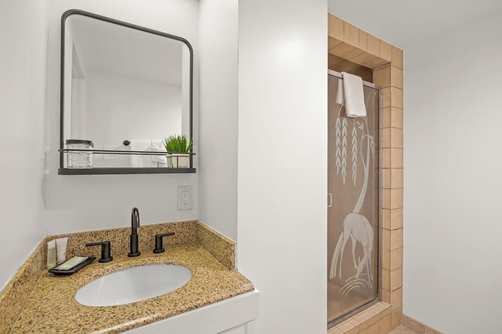 A bathroom with a granite countertop sink, a mirror, and a shower with a glass door.