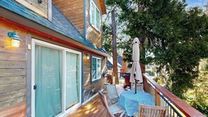 A wooden deck with a table and chairs, a covered patio area, and a view of trees. - Mountain-view cabin with fireplace, outdoor dining, firepit & wraparound deck (Lake Arrowhead)
