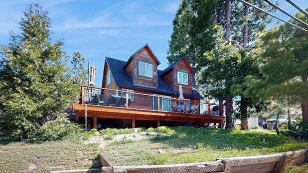 A two-story wooden house with a balcony, surrounded by trees and a grassy yard. - Mountain-view cabin with fireplace, outdoor dining, firepit & wraparound deck (Lake Arrowhead)