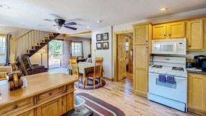 A kitchen with wooden cabinets, a white stove, and a dining area with a table and chairs. - Mountain-view cabin with fireplace, outdoor dining, firepit & wraparound deck (Lake Arrowhead)