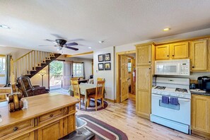 A kitchen with wooden cabinets, a white stove, and a dining area with a table and chairs. - Mountain-view cabin with fireplace, outdoor dining, firepit & wraparound deck (Lake Arrowhead)