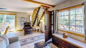 A living room with a staircase, a sofa, a coffee table, and a window with a view. - Mountain-view cabin with fireplace, outdoor dining, firepit & wraparound deck (Lake Arrowhead)