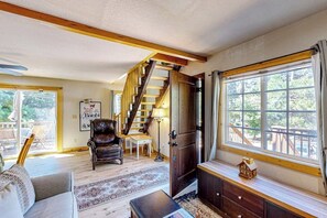 A living room with a staircase, a sofa, a coffee table, and a window with a view. - Mountain-view cabin with fireplace, outdoor dining, firepit & wraparound deck (Lake Arrowhead)