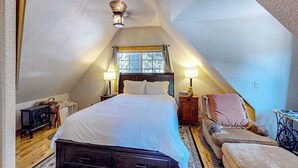 A bedroom with a sloped ceiling, a bed, two bedside lamps, a chair, a small table, and a heater. - Mountain-view cabin with fireplace, outdoor dining, firepit & wraparound deck (Lake Arrowhead)