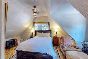 A bedroom with a sloped ceiling, a bed, two bedside lamps, a chair, a small table, and a heater. - Mountain-view cabin with fireplace, outdoor dining, firepit & wraparound deck (Lake Arrowhead)