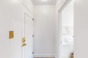 A white door with a brass handle and a gold plate, leading to a room with white walls and a wooden floor.