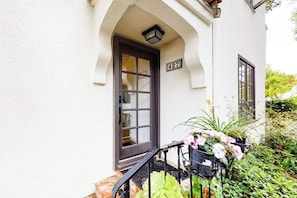 A white building with a dark door, a number '427' sign, and a small balcony with potted plants.
