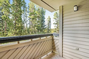 Ein Holzbalkon mit Geländer, der auf einen bewaldeten Bereich blickt.