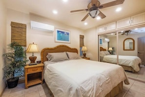 Ein Schlafzimmer mit einem großen Bett, einem Deckenventilator, einer Wandklimaanlage, einem Topf mit Pflanze und einem gerahmten Bild.