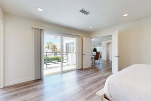 A spacious bedroom with a large bed, a sliding glass door leading to a balcony, and a view of the outside. - Dog-friendly two-story home with two kitchens, fast WiFi, patio, & gas grill (Newport Beach)