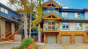 A two-story house with a balcony, a garage, and a small front yard with trees and shrubs. - Lovely Townhouse in Prime Location w/Shared Pool, Hot Tub - Near Downtown/Lifts (Breckenridge)