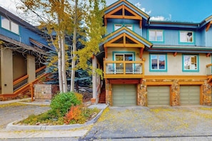 A two-story house with a balcony, a garage, and a small front yard with trees and shrubs. - Lovely Townhouse in Prime Location w/Shared Pool, Hot Tub - Near Downtown/Lifts (Breckenridge)