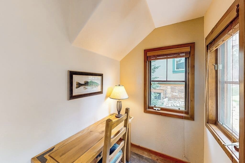 A corner room with a wooden bench, a framed picture, a lamp, and a window with a view of a stone building.