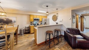 A modern kitchen with wooden cabinets, a central island with stools, a microwave, and a refrigerator. - Lovely Townhouse in Prime Location w/Shared Pool, Hot Tub - Near Downtown/Lifts (Breckenridge)