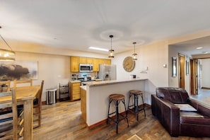 A modern kitchen with wooden cabinets, a central island with stools, a microwave, and a refrigerator. - Lovely Townhouse in Prime Location w/Shared Pool, Hot Tub - Near Downtown/Lifts (Breckenridge)