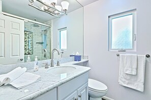 Une salle de bain avec un lavabo en marbre, des toilettes, un grand miroir et une fenêtre à vitres dépolies.
