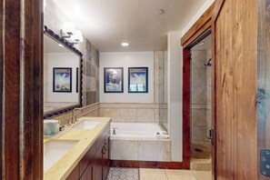 Une salle de bain avec deux lavabos, une baignoire et une douche. Des tableaux encadrés ornent le mur.