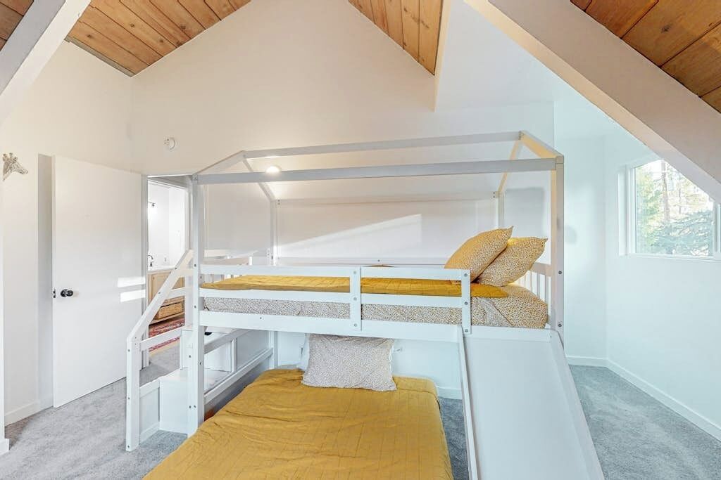 A bunk bed room with a wooden ceiling, white walls, and a window.