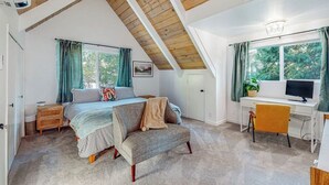 Une chambre avec un plafond en pente, un lit, un bureau, une chaise et une fenêtre avec des rideaux.