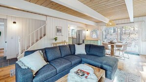Un salon moderne avec un canapé d’angle, un plafond en bois et une vue sur l’extérieur.
