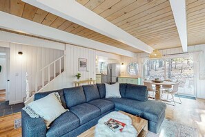 Ein modernes Wohnzimmer mit einem Ecksofa, Holzboden und Blick ins Freie.