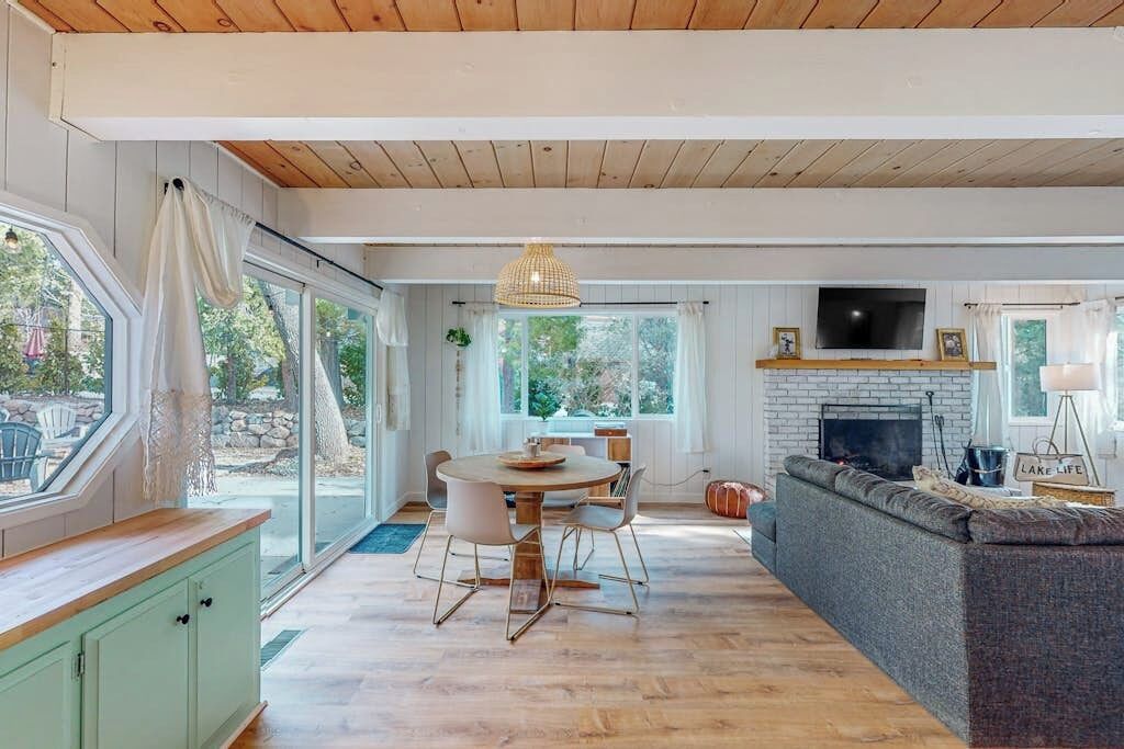 Amplia sala de estar con chimenea, una mesa de comedor con sillas y un gran ventanal con vista a un jardín.