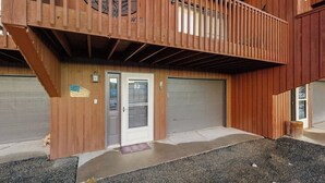 En tvåvåningsbyggnad i trä med en balkong, två garageportar och en välkomstmatta.