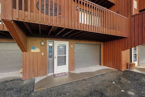 Ein zweigeschossiges Holzhaus mit Balkon, zwei Garagentoren und einer Fußmatte.