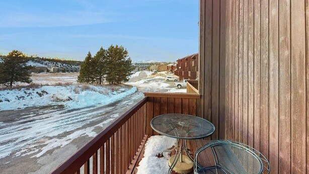 En balkong med utsikt över ett snötäckt landskap, ett träräcke och två metallstolar.