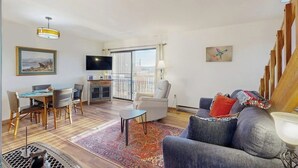 Ett vardagsrum med en soffa, ett matbord med stolar, en tv och en balkong med utsikt.